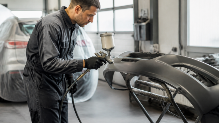 Garagiste appliquant de la peinture sur un pare choc de voiture dans un garage